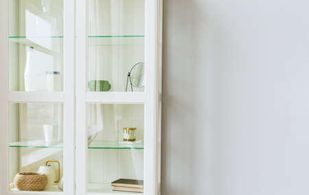 Cabinet filled with decoration elements stay against a gray wall. Glass door. White wood.の写真素材