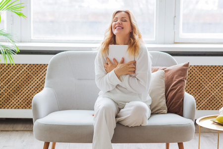 A woman in white clothes reads on the couch at home and hugs a piece of paper with her wishes. Desire visualization conceptの写真素材