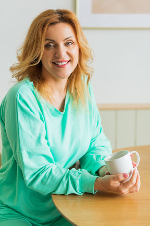 Woman in kitchen with cup of hot drink, morning routine, self reflection. Social media and digital...
