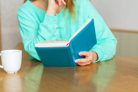 Mature woman drinking tea from cup and writing down thoughts or ideas in notebook and planning her...