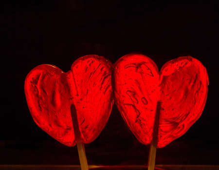 Two red heart-shaped lollypop shot over black background. Horizontal photoの写真素材