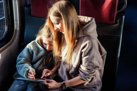 Mom helps her daughter draw a picture while they are on the trainの写真素材