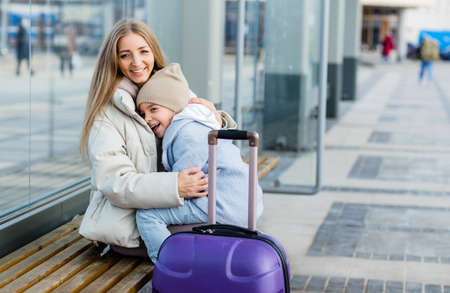 Mom and daughter are sitting at the bus stop, waiting for the bus and huggingの写真素材