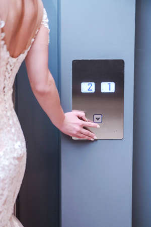 Bride in white wedding dress presses the elevator buttonの写真素材