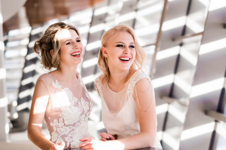 Two blonde model girls posing in wedding dresses in the interior flooded with sunlightの写真素材
