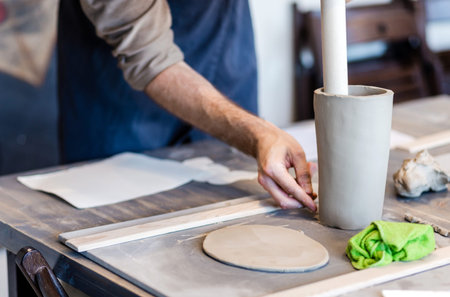 A young potter is engaged in crafts in his workshop, making a vase from clay, shaping it
