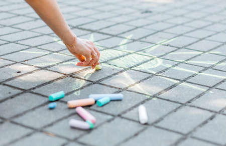 girl paints a yellow  sun with colored chalk on asphalt outdoorsの写真素材