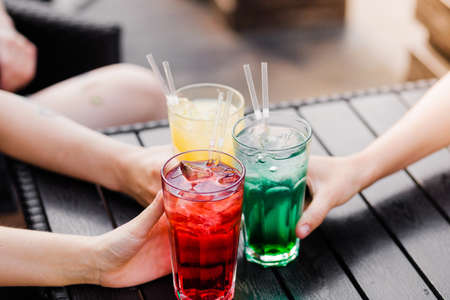 Company on the three party girls clinking glasses with each other with cocktails of yellow, red and green colorの写真素材