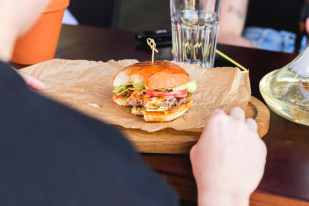 Young female hands are holding a bitten hamburger in a fast food restaurant.