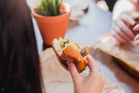 Young female hands are holding a bitten hamburger in a fast food restaurant.の写真素材