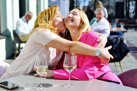Two beautiful adult blonde women met at a table in a cafe and hug when they meet. Horizontal photoの写真素材