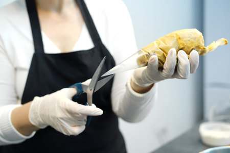 A woman confectioner cuts off the tip of a pastry bag with cream for further use. Horizontal photo