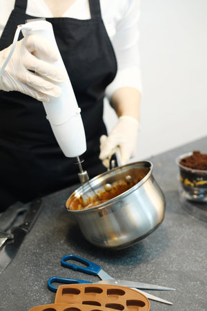 Woman confectioner with a mixer beats chocolate cream for making dessert. Vertical photo