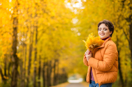 Cheerful young girl with short brown hair wearing autumn yellow jacket, walking at the park. Autumn...