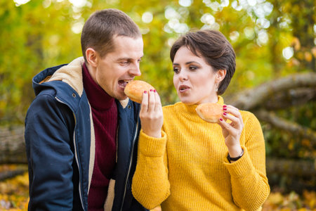 A man and a woman eat sandwiches at an autumn picnic. Horizontal photo