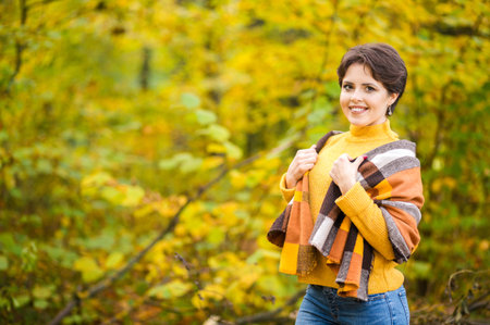 Cheerful smiling young brunette wrapped in blanket in autumn forest. Horizontal photoの写真素材