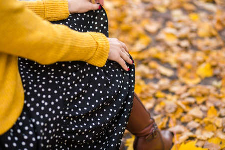 Autumn fashion. The girl is sitting in a black polka-dot skirt, a yellow knitted sweater and boots. Horizontal photoの写真素材