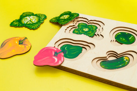 Children educational game for children from wooden figures of vegetables on a yellow background. Horizontal photoの写真素材