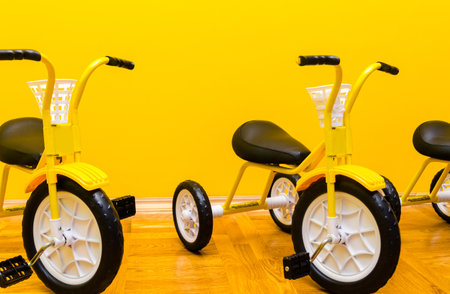 Children yellow bicycles stand in a row against a yellow wall in a kindergarten. Horizontal photoの写真素材