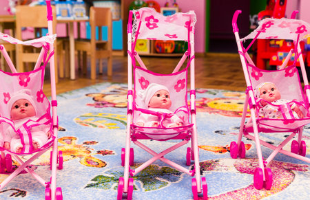 Three dolls are sitting in pink toy carriages. Playroom in kindergarten. Horizontal photoの写真素材