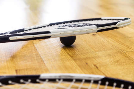 A black squash ball lies under a tennis racket on a parquet floor. Horizontal photoの写真素材