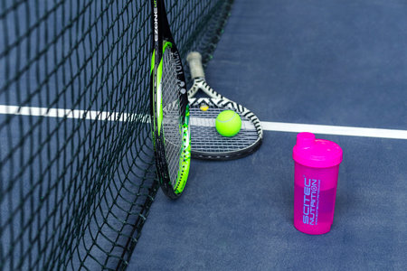 Tennis rackets, water bottle and ball against a stretched tennis net on an indoor tennis court. Horizontal photo. Minsk, Belarus - May 25, 2022のeditorial素材