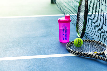 Tennis rackets, water bottle and ball against a stretched tennis net on an indoor tennis court. Horizontal photo. Minsk, Belarus - May 25, 2022のeditorial素材