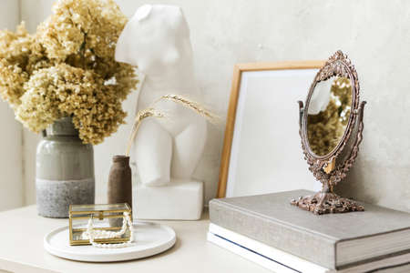 A bouquet of dry hydrangea flowers, books, a mirror, a Greek statue stand on a table against a light wall. Autumn mood in the interior. Horizontal photoの写真素材