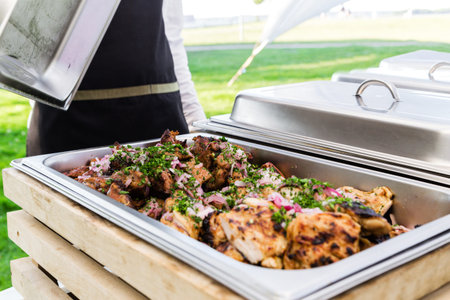 In a metal steamer BBQ pork with onions. Summer picnic. Catering job. Horizontal photo