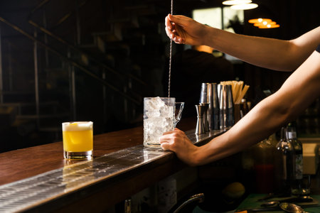 The bartender uses a bar spoon to stir the ice in a glass to cool it faster. Horizontal photo