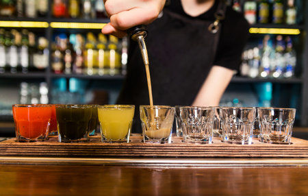 The bartender at the bar pours red tincture into shots. Horizontal photo