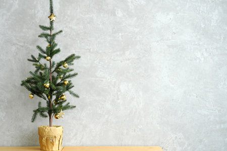 Christmas tree with golden balls stands in a pot against a gray wall. Horizontal photoの写真素材