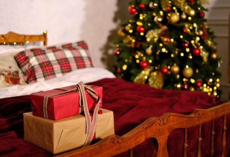 Christmas gifts tied with a ribbon lie on the bed against the backdrop of the Christmas tree. Horizontal photoの写真素材