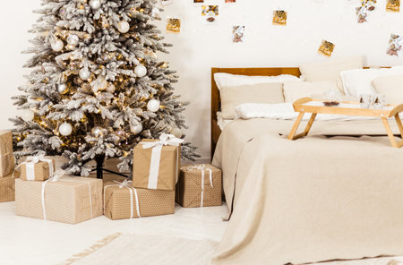 New Years bright interior bedroom with decorated Christmas tree with garlands, white bed, beige blanket, photos on the wall. Christmas interior. Scandinavian style. Horizontal photoの写真素材