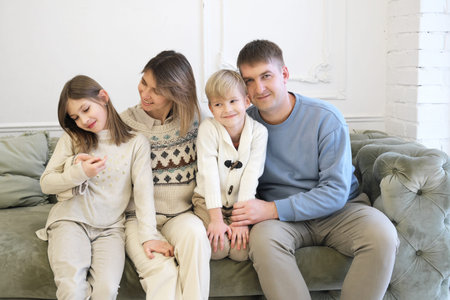 A family of four pose on a sofa in a living room Christmas decor. Family smiling and looking at the...