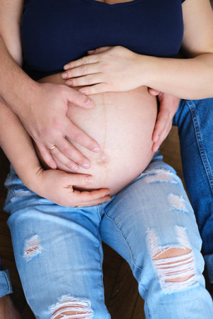 Closeup of young man touching pregnant wife's belly. Vertical photoの写真素材