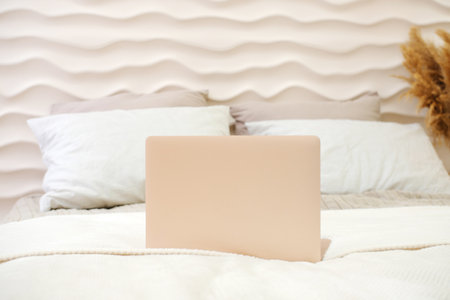New laptop on bed blanket in home bedroom interior in beige and with smooth lines. Horizontal photoの写真素材