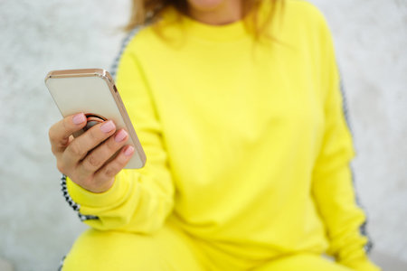 A woman in a yellow tracksuit holds a mobile phone in her hands. The concept of two future mobile...