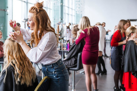 Competition stylists hairdressers at the exhibition of hairstyles and makeup. Hairdresser creates hairstyle for his model. Minsk, Belarus - April 10, 2022. Horizontal photoのeditorial素材