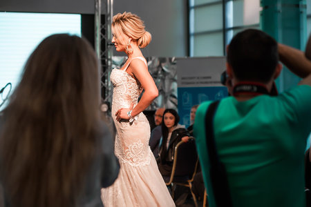 A model in a wedding dress with hair and make-up walks down the catwalk. Journalists take pictures of the model. Minsk, Belarus - April 10, 2022. Horizontal photoのeditorial素材