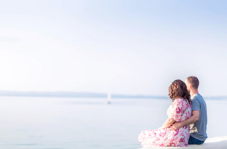 A young couple, a guy and a girl, are sitting on the shore of the lake and looking into the distance. Couple in love, valentine's day. Horizontal photoの写真素材