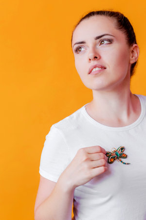Girl in a white t-shirt posing with a brooch shape of dragonfly with blue green gemstone imitation...