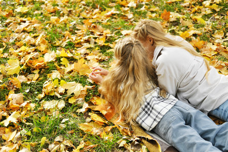 The family has fun in the park. The girl and mother lie on a blanket with their backs to the camera and look at the autumn leaves. Horizontal photoの写真素材