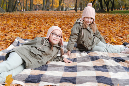 Two twin sisters lie on a blanket in the autumn park. Horizontal photoの写真素材