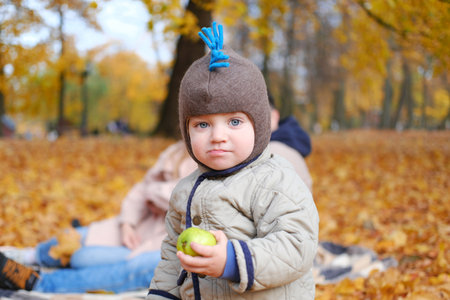 Cute stylish child boy wear casual clothes jacket and pants in park with fallen leaves outdoor eat apple. Autumn season. Horizontal photoの写真素材