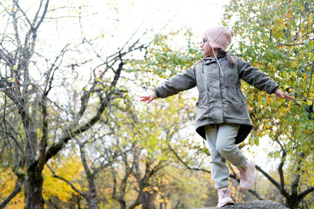 A cute girl climbed a high stone in an autumn apple orchard and showing an airplane with her hands....