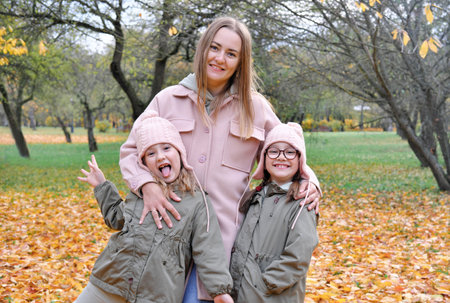 Caucasian family play in autumn park, mother embrace two girls twins and smile, active weekend outdoors. Horizontal photoの写真素材