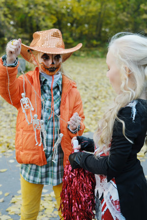 Girl child in an orange jacket and a cowboy hat shows her friend in a cheerleader costume her...