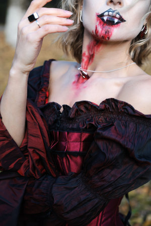A woman in the image of a vampire or a witch with white make-up and in a medieval dress poses in the forest in front of the camera. Vertical photoの写真素材