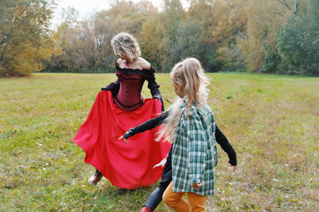 The family celebrates Halloween. Mom in the form of a vampire, girls in the form of a cheerleader and a pumpkin. Mom plays with her daughters. Horizontal photoの写真素材